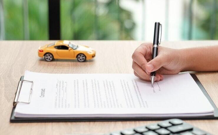 woman signing car loan agreement contract with car toy calculator wooden desk 43919 4141 e1748919051172
